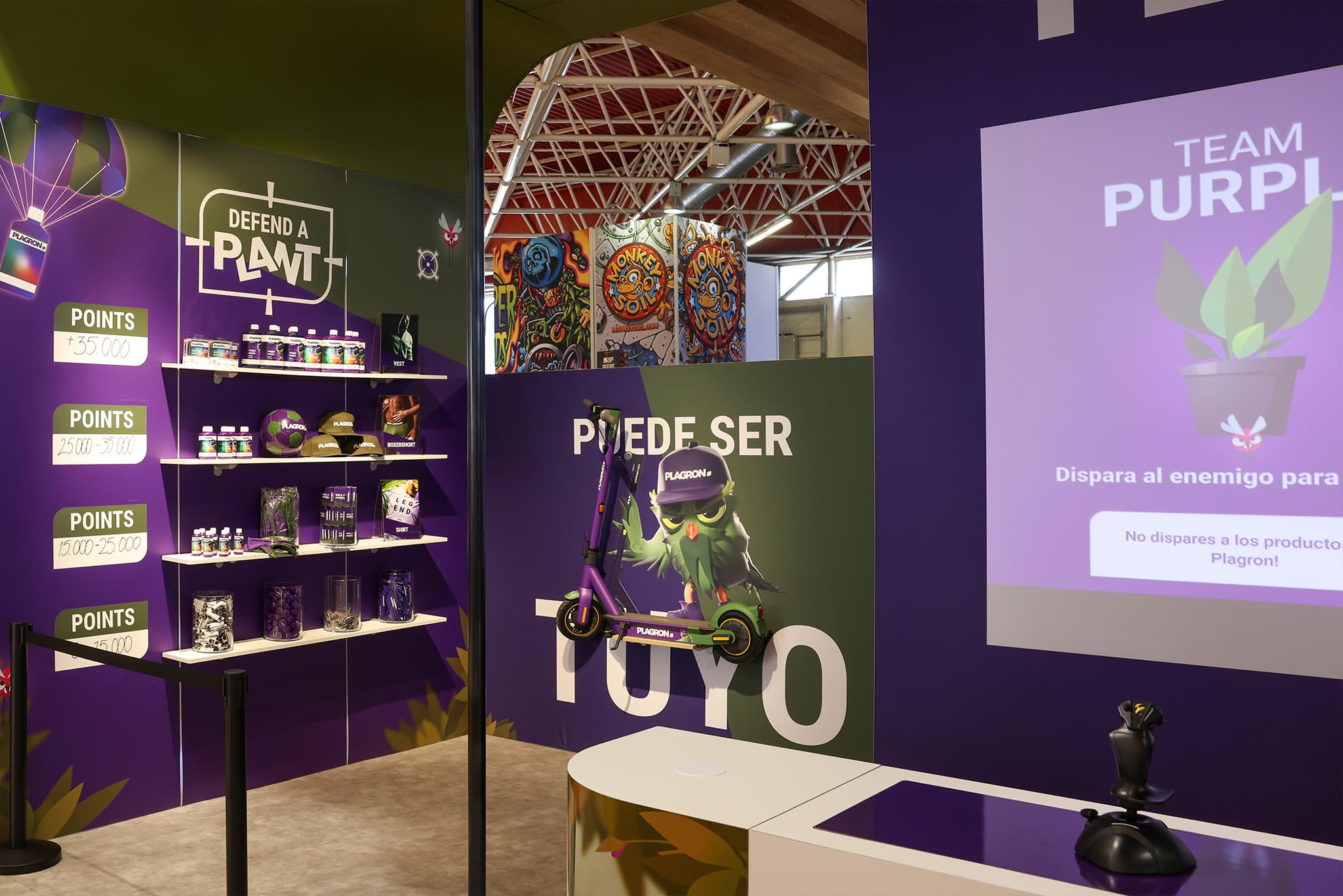 The prize wall: merch is tiered by the points scored in a round, from stickers and pins up to a full 35,000+ point bundle. A physical joystick sits ready on the counter.