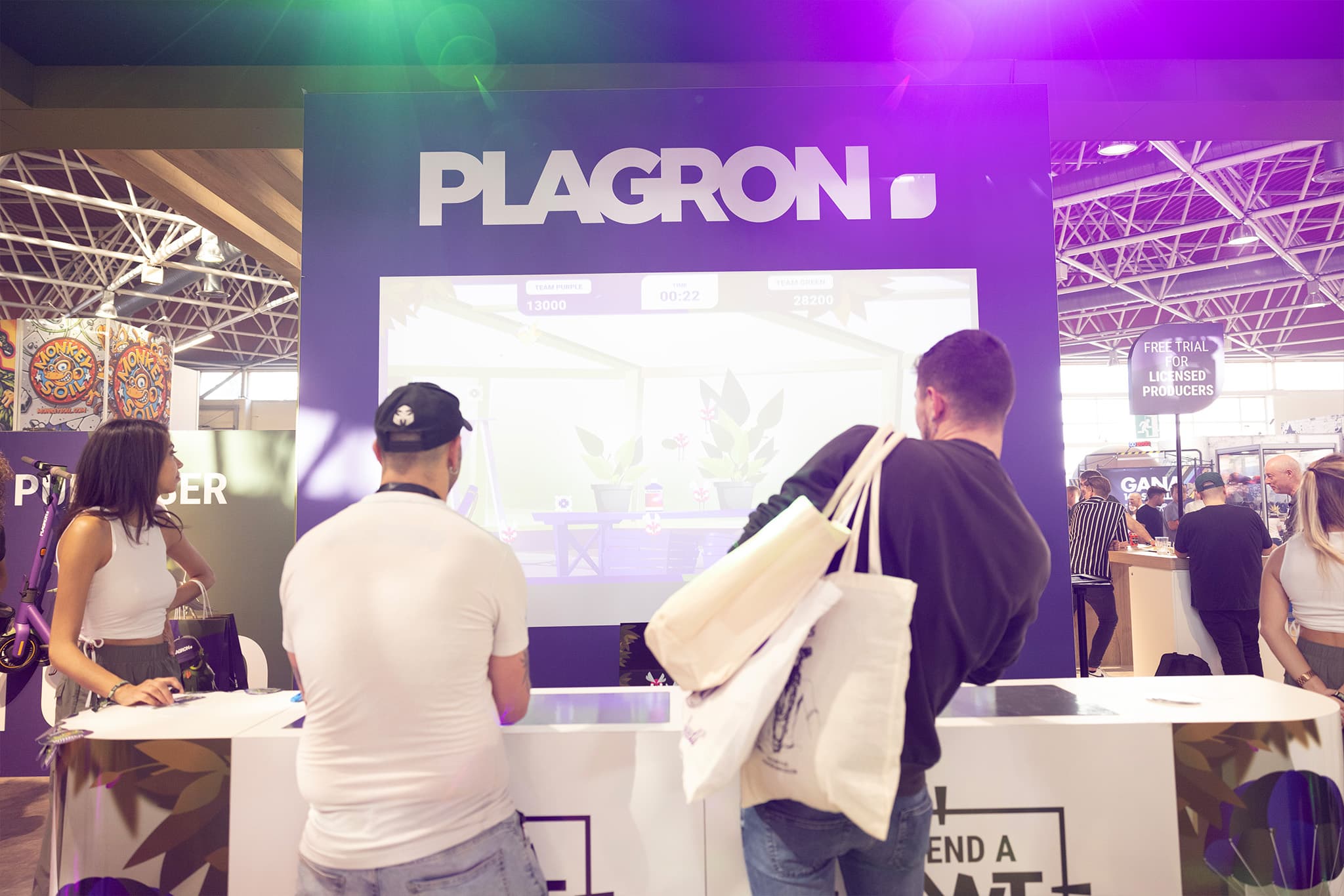 Two more visitors at the booth, Team Purple vs Team Green scoreboard visible on the big screen.