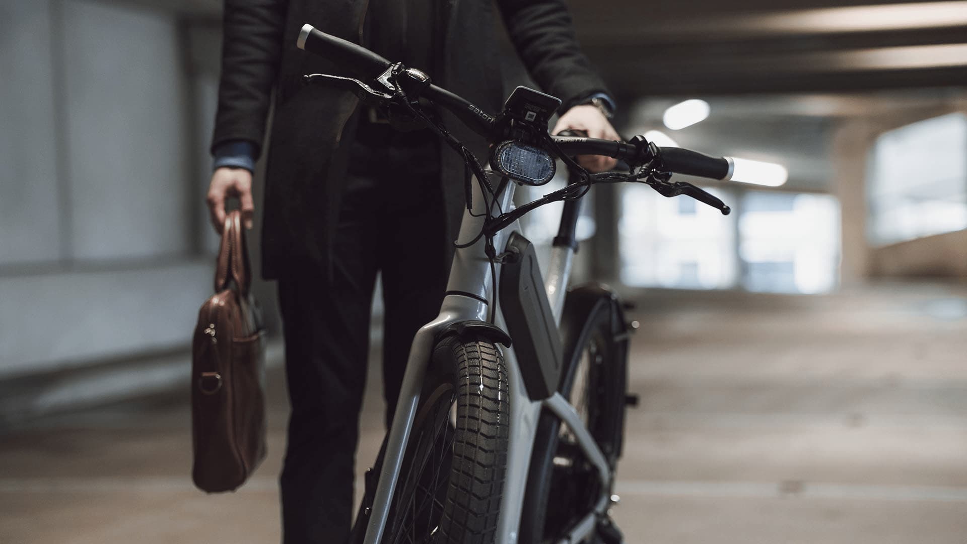 A commuter with a leather work bag walking the Byqr through the parking garage.